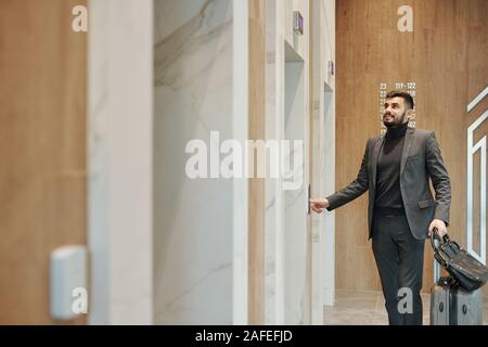 Contemporary business traveler in suit pushing elevator button on the wall Stock Photo