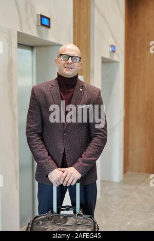 Bald successful businessman in suit waiting for elevator in hotel lounge Stock Photo