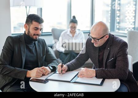 Two successful business partners signing financial documents in hotel lounge Stock Photo