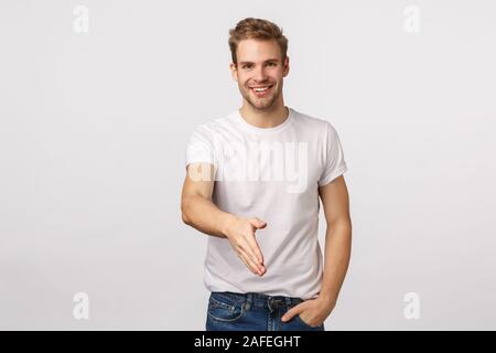 Nice to meet you. Attractive and confident, smiling blond man went interview, applying job, greeting new coworkers, extend arm forward to give Stock Photo