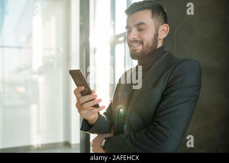 Happy young businessman scrolling in smartphone and looking through contacts Stock Photo