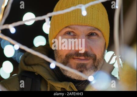 Portrait of mature bearded man looking through the Christmas lights Stock Photo
