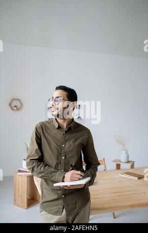 Young pensive office worker thinking of ideas and writing them down in notebook Stock Photo