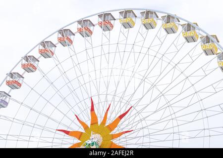 White ferris wheel with colorful cabins and star decoration in the middle of the wheel in the background of cloudy sky Stock Photo