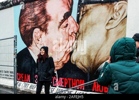 Young female posing in front of Dmitri Vrubel's famous mural on Berlin Wall at East Side Gallery in Berlin, Germany