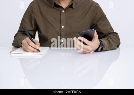 Hands of young businessman with smartphone and pen writing down working plan Stock Photo
