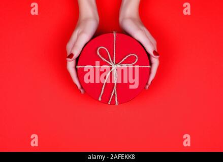 Closed red round gift box on red background. the view from the top. Gift for the holidays of New Year, Christmas, Valentine's day, March 8. Stock Photo
