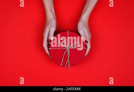 Closed red round gift box on red background. the view from the top. Gift for the holidays of New Year, Christmas, Valentine's day, March 8. Stock Photo