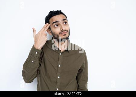 Perplexed young man in casualwear holding two fingers by his head Stock Photo