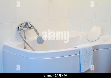 Modern corner bathtub with headrest, faucet and shower with a long hose in the snow-white interior bathroom, selective focus Stock Photo