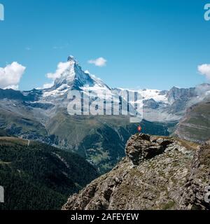 Hiker in bright red jacket taking in the Alpine scenery around the famous Matterhorn mountain