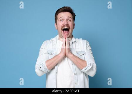 Emotional excited young man exclaiming in shock and full disbelief, gesturing actively. Positive facial human emotions, feeling. Studio shot Stock Photo