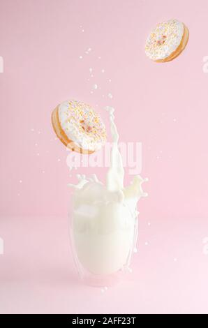 Splashing glass of milk and flying donuts with sprinkles on pink background. Copy space. Levitation food concept. Stock Photo
