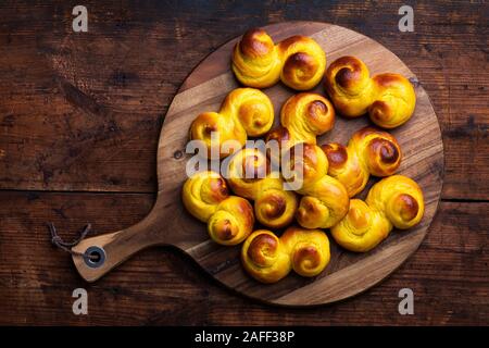 Freshly baked homemade Swedish traditional s-shaped saffron buns, also known as lussebullar or saffransbröd on a round chopping board. Seen from above