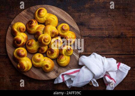 Freshly baked homemade Swedish traditional s-shaped saffron buns, also known as lussebullar or saffransbröd. Seen from above flat lay on a dark wooden Stock Photo
