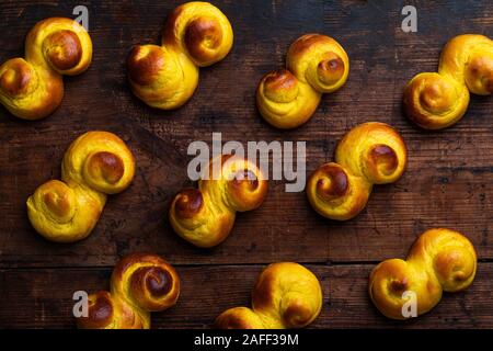 A background of Swedish traditional christmas bun Lussekatter or Lussebullar on a rustic wooden table. The buns are freshly made and homemade and the Stock Photo