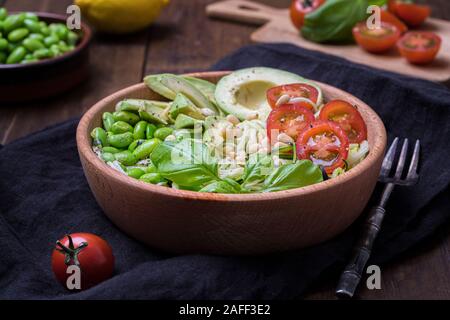 Side view of a fresh, healthy salad with zoodles zucchini noodles, baby tomatoes, avocado and edamame beans. The salad is in a wooden bowl on a dark b Stock Photo