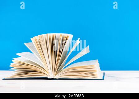 Composition with vintage old hardback books, diary, fanned pages on wooden deck table and blue background. Stacking books. Back to school. Copy space Stock Photo