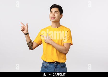 Dreamy handsome and upbeat young creative asian male student, have interesting ideas, pointing and looking upper left corner, see pleasant offer Stock Photo