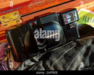 A retro film camera lays on leather gloves in a wooden footlocker. Car keys on a swiss army key chain lay on the edge of the frame. Stock Photo