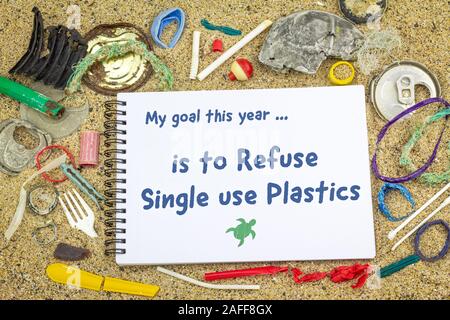 This year I will to stop using single use plastic handwritten on notebook surrounded by real plastic pollution in sand on beach. New Years resolutions Stock Photo