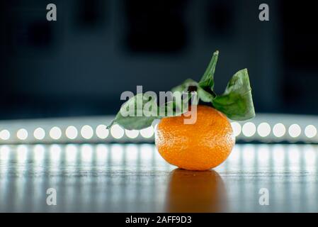orange Mandarin with green leaves on the table lit with lights new year holiday Stock Photo