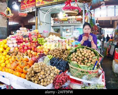 A trader checks her mobile phone with fruit and vegetables for sale at a market stall in Phnom Penh, Cambodia Stock Photo