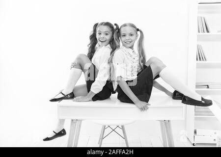 Rebellious spirit. School club. Little schoolgirls classmates friendly kids. Schoolgirls friends sit on desk. Best friends relaxing. Schoolgirls tidy hairstyle relaxing having rest. School uniform. Stock Photo