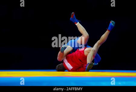 Two men in blue and red sambo wrestling on a yellow wrestling carpet in the gym Stock Photo
