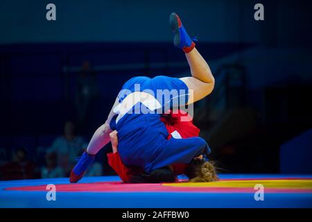 Two woman in blue and red wrestling on a yellow wrestling carpet in the gym Stock Photo
