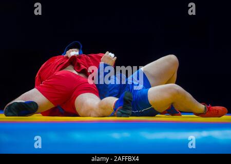 Two men in blue and red wrestling on a yellow wrestling carpet in the gym Stock Photo