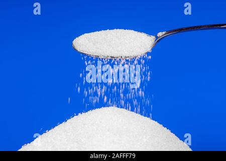 Falling sugar from a spoon on a blue background Stock Photo