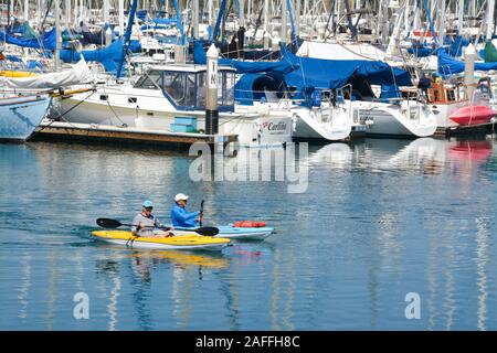 A fit, middle aged couple maneuvers their kayaks around the docked sailboats and yachts in the marina at the Santa Barbara harbor, Santa Barbara, CA Stock Photo