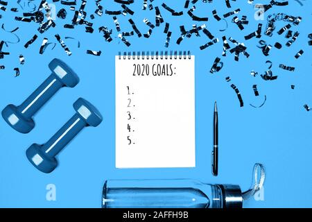 Goals list for New Year Holiday. Christmas sport set with dumbbells, notebook with pen, bottle of waterwater and colorful confetti on classic blue color background. Flat lay, top view, copy space. Stock Photo