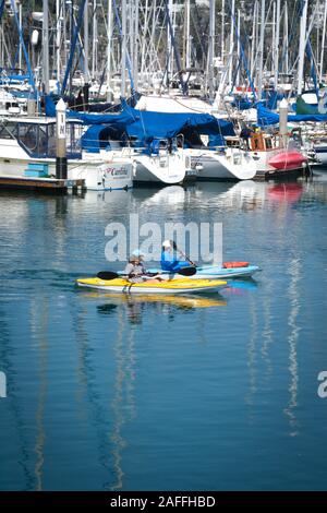 A fit, middle aged couple maneuvers their kayaks around the docked sailboats and yachts in the marina at the Santa Barbara harbor, Santa Barbara, CA Stock Photo