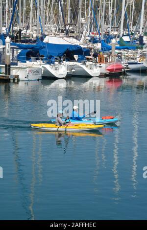 A fit, middle aged couple maneuvers their kayaks around the docked sailboats and yachts in the marina at the Santa Barbara harbor, Santa Barbara, CA Stock Photo