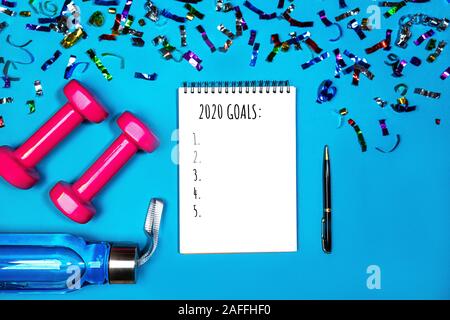 Goals list for New Year Holiday. Christmas sport set with dumbbells, notebook with pen, bottle of waterwater and colorful confetti on mint green blue color background. Flat lay, top view, copy space. Stock Photo