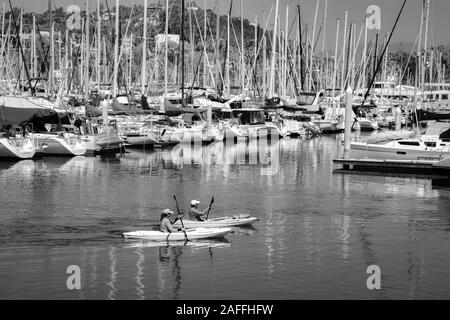 A fit, middle aged couple maneuvers their kayaks around the docked sailboats and yachts in the marina at the Santa Barbara harbor, Santa Barbara, CA, Stock Photo