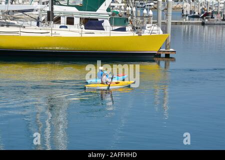 A fit, middle aged couple maneuvers their kayaks around  docked sailboats and yachts in the marina at the Santa Barbara harbor, Santa Barbara, CA Stock Photo