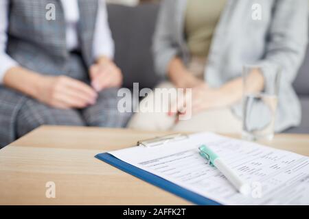 Close up of medical form lying on table with two women discussing issues during therapy session in background, copy space Stock Photo