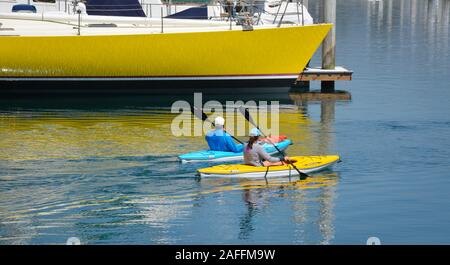 A fit, middle aged couple maneuvers their kayaks around  docked sailboats and yachts in the marina at the Santa Barbara harbor, Santa Barbara, CA Stock Photo