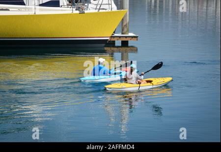 A fit, middle aged couple maneuvers their kayaks around  docked sailboats and yachts in the marina at the Santa Barbara harbor, Santa Barbara, CA Stock Photo