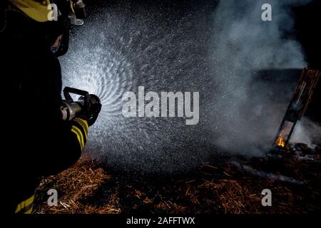 Group of firemen in protective suits putting out a fire with a water hose Stock Photo