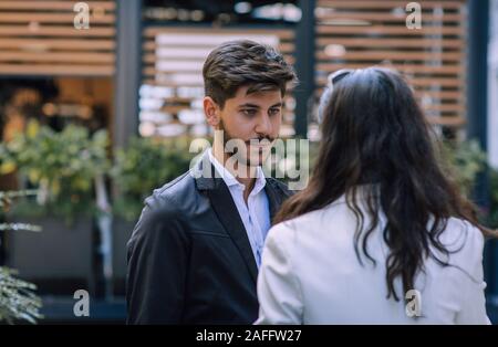Positive team members discussing project during outdoor break. Two coworkers walking near office building, smiling and talking. Business communication Stock Photo