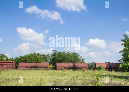 Abandoned wagons, old and rusty tank cars that used to carry oil, on display on a decommissioned railway train track that was left unused since the ec Stock Photo