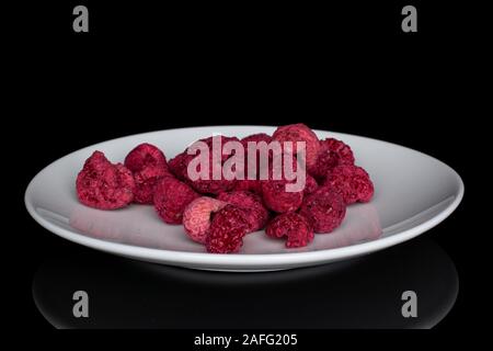 Lot of whole dried raspberry on white ceramic plate isolated on black glass Stock Photo