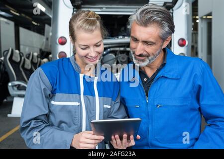 male and female mechanics looking at tablet in bus garage Stock Photo