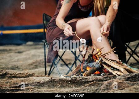 Cropped image of travelers using sticks when frying marshmallows on fire Stock Photo