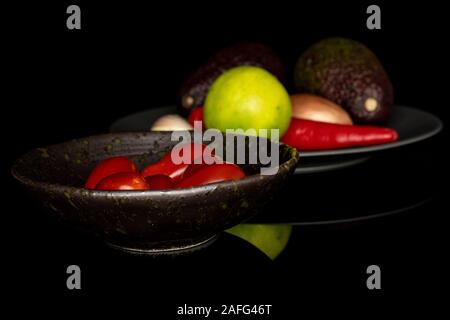 Lot of whole ingredient guacamole on gray ceramic plate in glazed bowl isolated on black glass Stock Photo