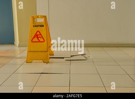 Closeup buckled and broken tiles on corridor near elevator with a caution sign for warning and protecting people from stepping on them Stock Photo